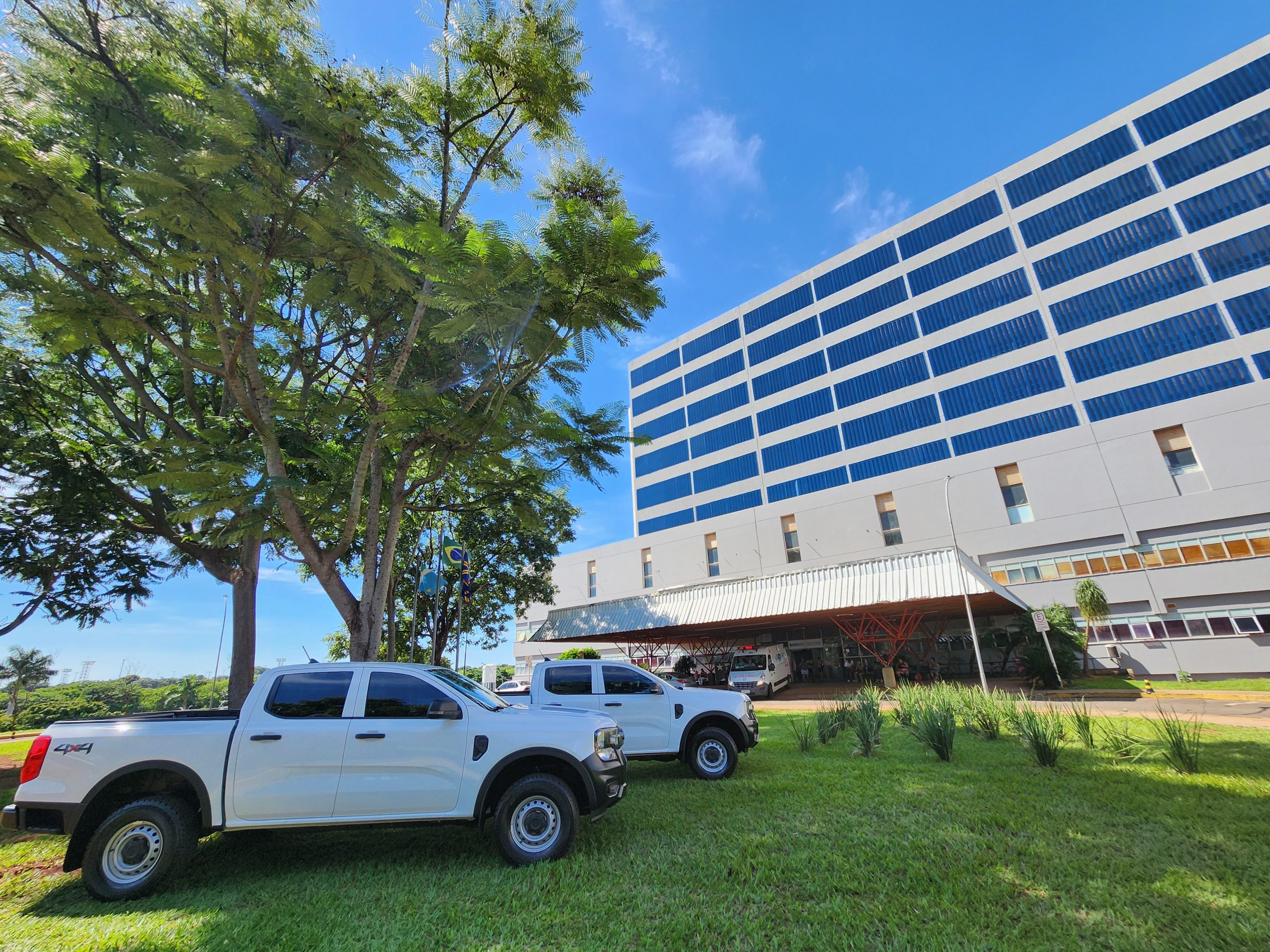 Duas caminhonetes brancas novas estacionadas no gramado em frente ao Hospital Regional de Mato Grosso do Sul, em Campo Grande